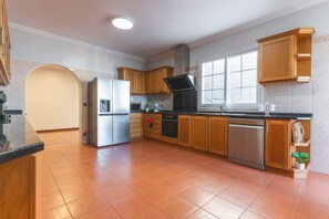 A modern kitchen with wooden cabinets, stainless steel appliances, and a large window providing natural light. - Villa Alves by Atlantic Holiday (Santana)