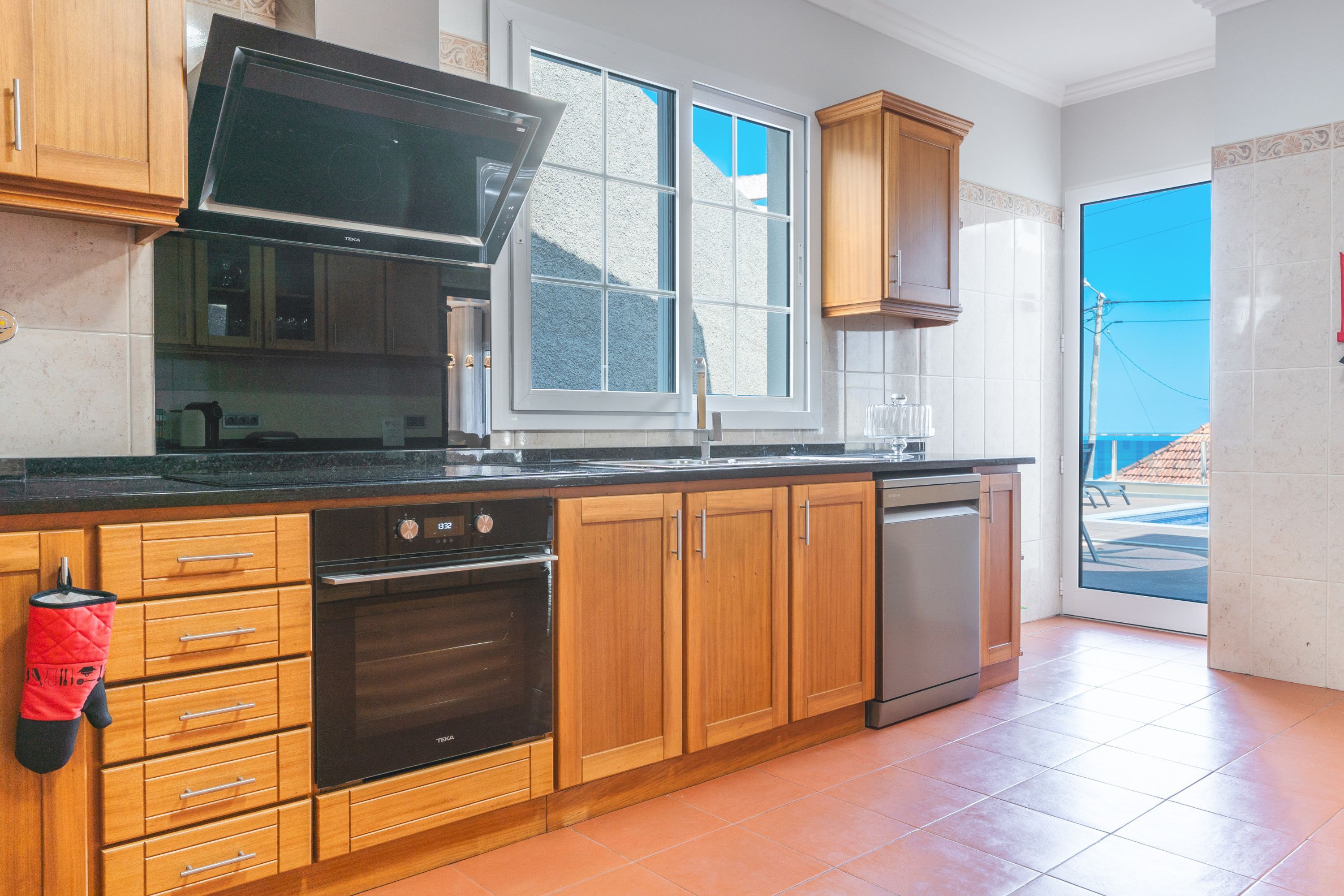 A kitchen with wooden cabinets, a black oven, a dishwasher, and a window with a view of the outside.