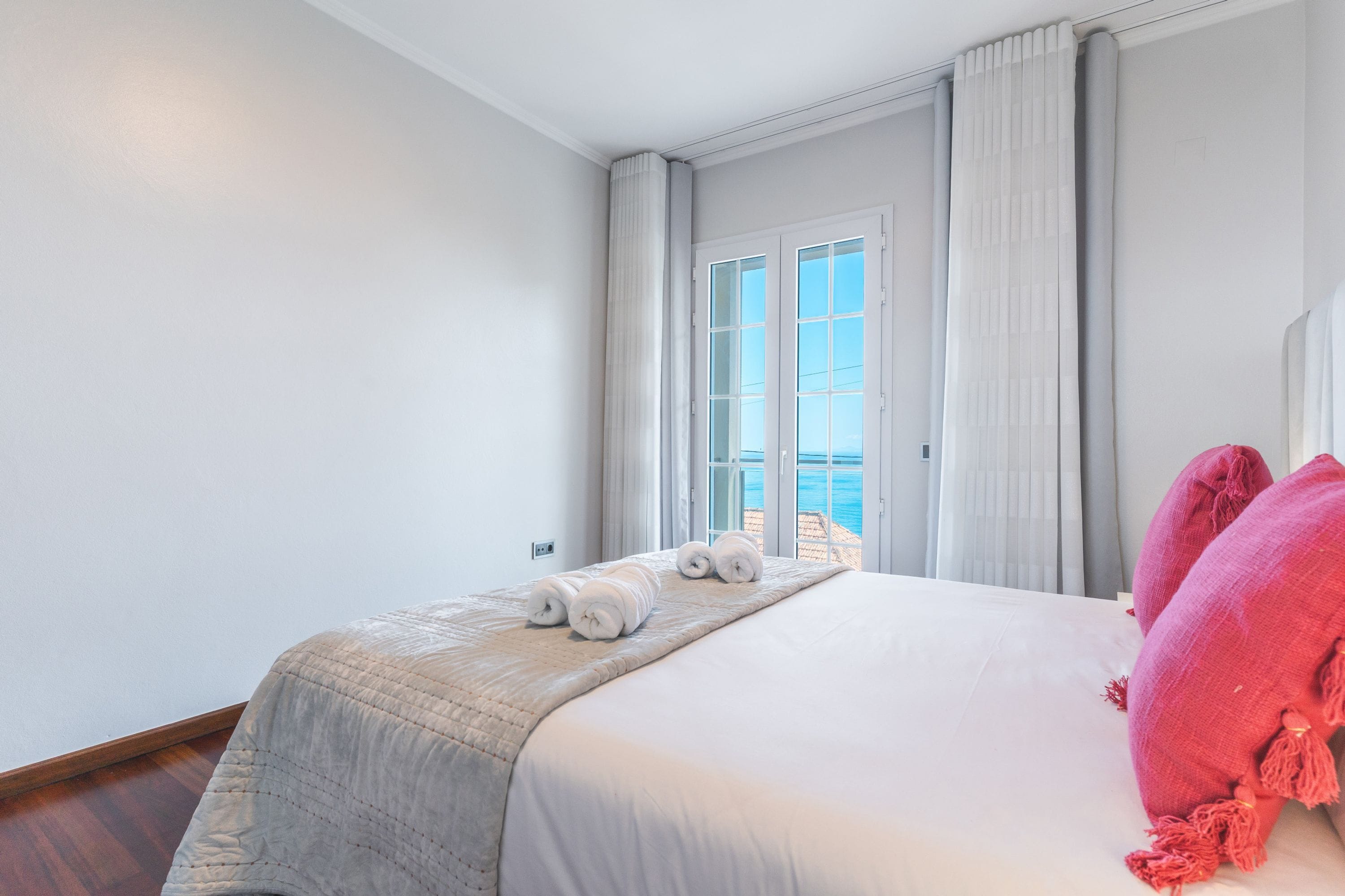 Habitación de hotel con una cama grande, vista al mar a través de una ventana y un balcón.