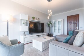 A modern living room with a flat-screen TV, white furniture, a coffee table, and a sofa with decorative pillows. - Villa Alves by Atlantic Holiday (Santana)