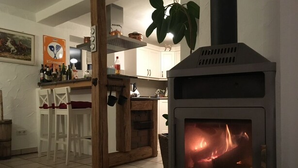 A kitchen with a wood-burning stove, white chairs, a bar area, and a hanging plant. - Apartment on a horse farm, children and pets welcome, garden & terrasse, grill (Lichtenau)