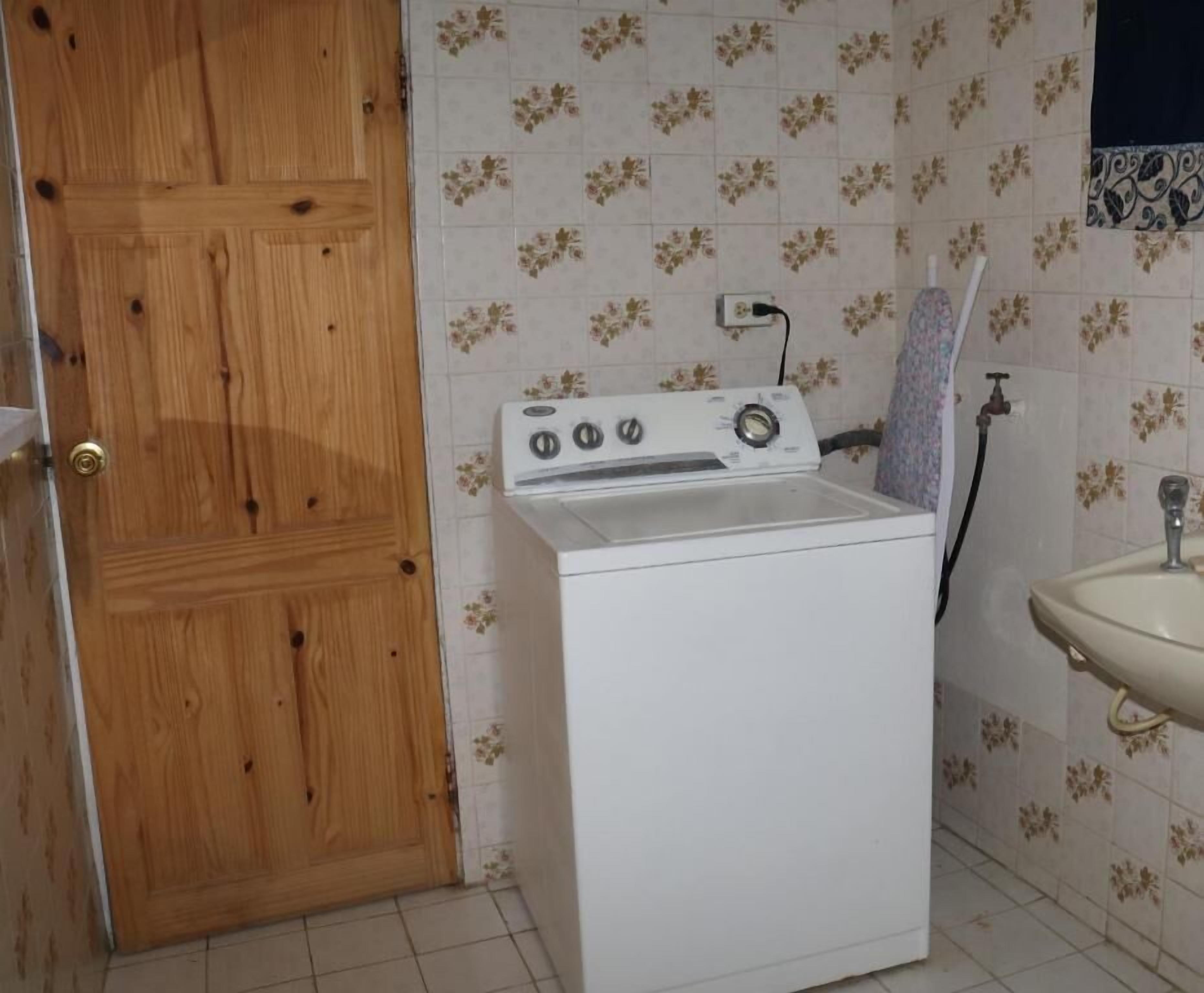 Un lavadero con una lavadora blanca, una puerta de madera y un lavamanos con azulejos florales.