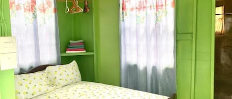 A room with a bed, green walls, a shelf with books, and a window with curtains.