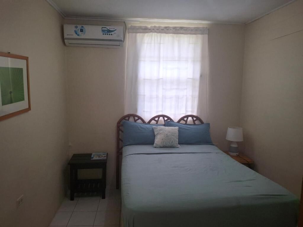 Un dormitorio pequeño y ordenado con una cama individual, una mesita de noche y una ventana con cortina translúcida.