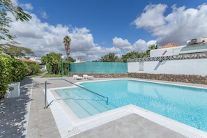 A swimming pool with a stone wall, a metal handrail, and a clear blue sky.