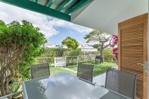 Un patio al aire libre con una mesa y sillas de vidrio, rodeado de vegetación y vistas del barrio.