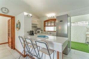 Una cocina con encimera blanca, taburetes de bar, refrigerador y microondas.