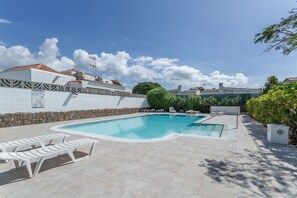 Una piscina con sillas de descanso, un muro de piedra y un cielo azul despejado.