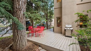 A patio with red chairs and a grill, surrounded by trees and a building. - Aspen Villas/bleeker Street Townhome 2 Plus Den (Aspen)