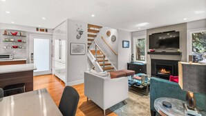 A modern living room with a fireplace, a TV mounted above it, and a staircase leading to another level. - Aspen Villas/bleeker Street Townhome 2 Plus Den (Aspen)