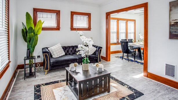Una sala de estar con un sofá negro, una mesa de centro y una planta grande. Se ve un comedor a través de un vano abierto.
