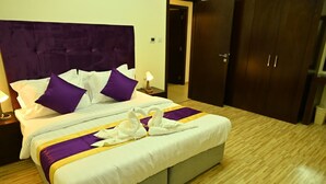 A neatly made bed with purple and white bedding, a pair of white towels arranged in a swan shape, and a wooden floor. - Aspire Tower (Manama)