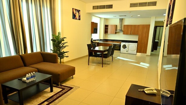 A modern living room with a sofa, coffee table, and a dining area with chairs. A kitchen is visible in the background with a washing machine. - Aspire Tower (Manama)