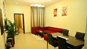 A modern living room with a red sofa, a coffee table, and a dining area with a table and chairs. There is a plant, a curtain, and artwork on the walls. - Aspire Tower (Manama)