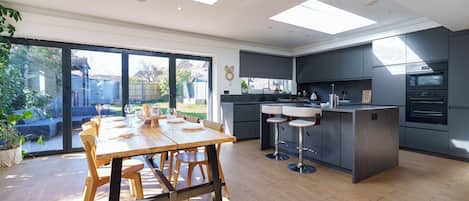A modern kitchen with a dining area, large windows, and a view of the backyard.