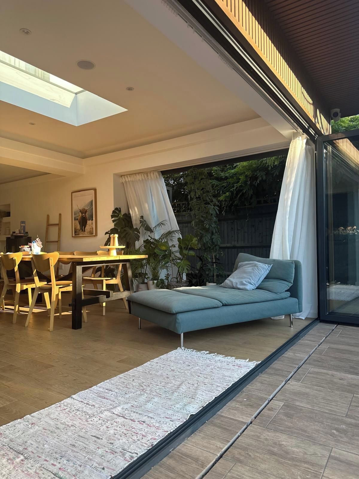 A modern interior with a dining area, a sofa, and a glass door leading to a garden.