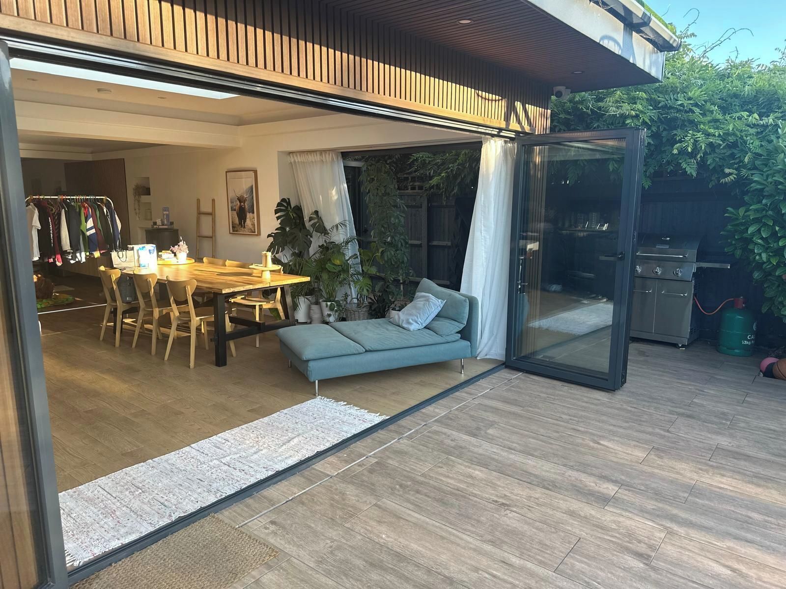 Un espace de vie à aire ouverte comprenant un coin repas, un canapé et une porte-fenêtre coulissante donnant sur un patio équipé d’un barbecue.