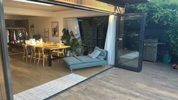 Un espace de vie à aire ouverte comprenant un coin repas, un canapé et une porte-fenêtre coulissante donnant sur un patio équipé d’un barbecue.