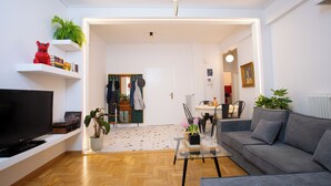 Ein modernes Wohnzimmer mit Flachbildfernseher, grauem Sofa, Couchtisch und Essbereich mit Tisch und Stühlen.