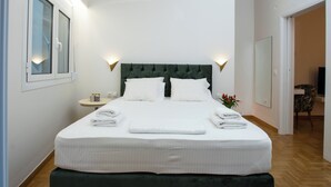 Ein ordentlich bezogenes Bett mit weißen Leinen und Kissen, ein grüner gepolsterter Kopfteil und ein Deckenventilator.