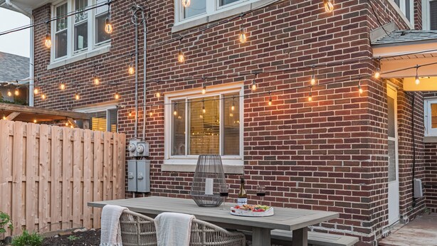 Ein Ziegelhaus mit einer Holzdachterrasse, Sitzgelegenheiten im Freien und Lichterketten.