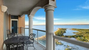 Un balcon avec une table et des chaises, donnant sur un paysage côtier avec de l’eau et de la végétation.