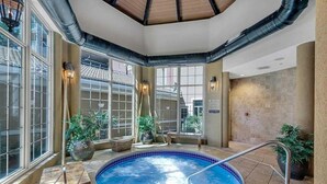 Une piscine intérieure avec vue sur l’extérieur, de grandes fenêtres et des plantes en pot.