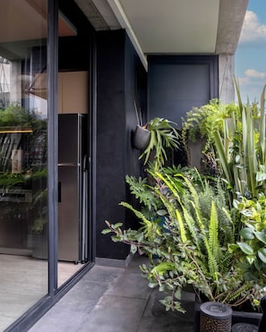 Um edifício moderno com entrada por porta de vidro, uma parede preta e diversos vasos de plantas em seu interior.