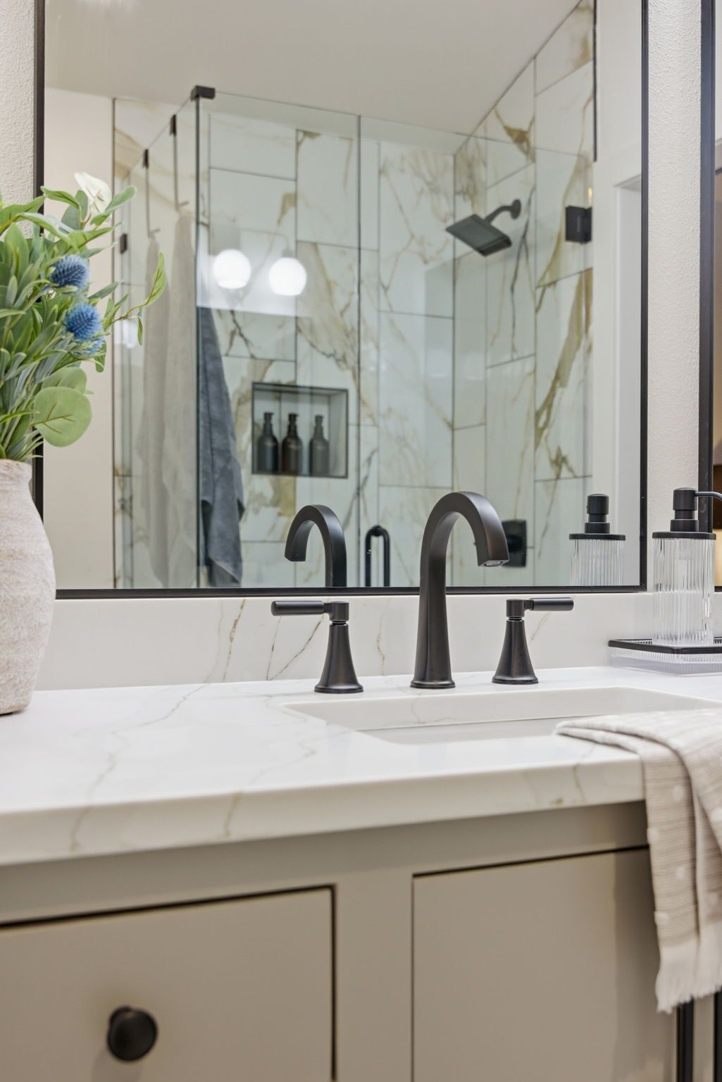 A bathroom with a marble sink, a large mirror, and a shower with a glass enclosure.