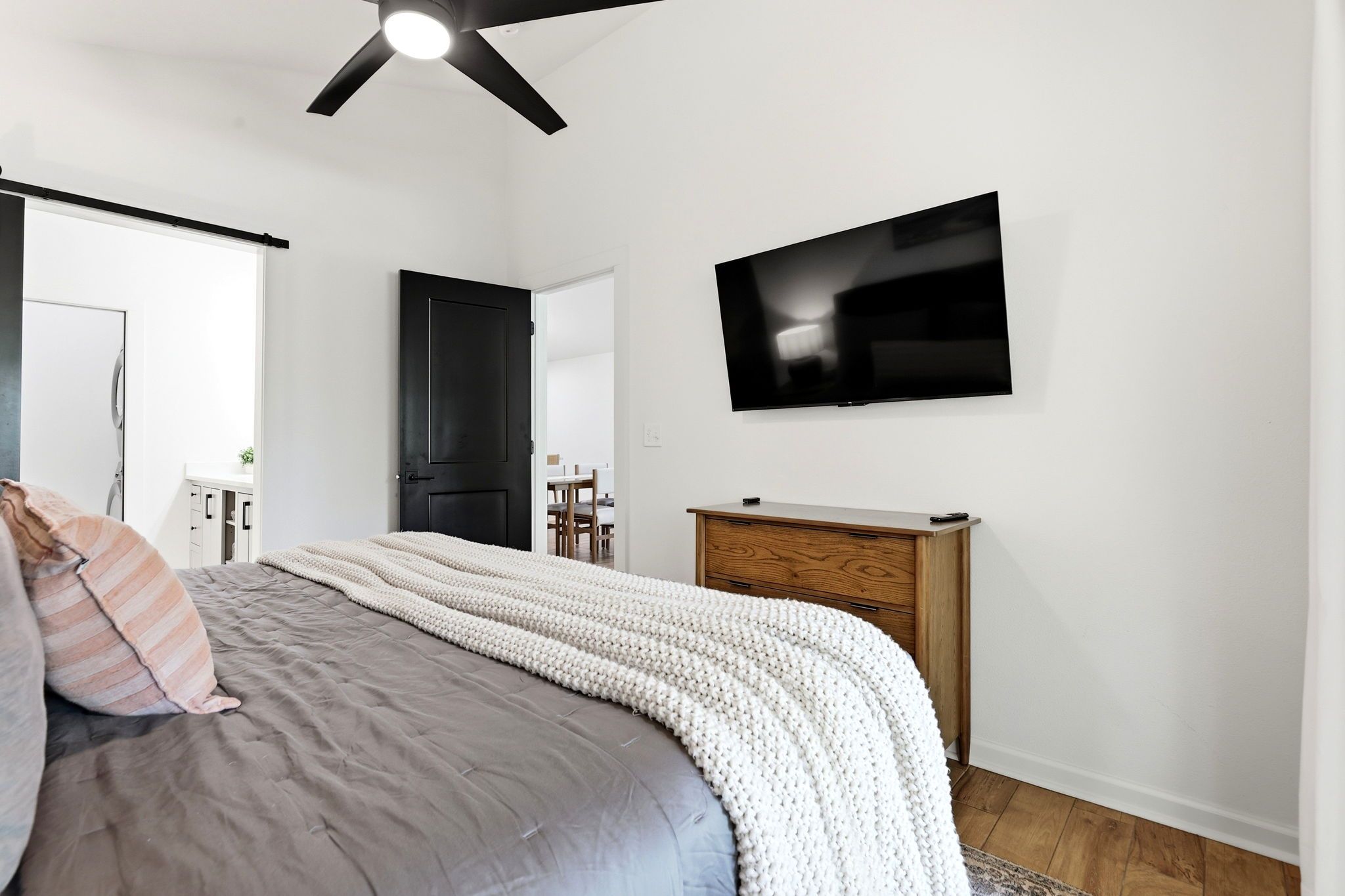 Quarto com cama, televisão fixada na parede e ventilador de teto.