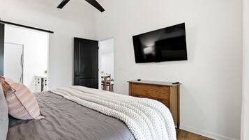 Quarto com cama, televisão fixada na parede e ventilador de teto.