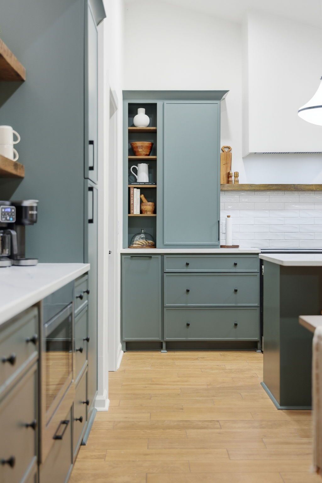 A modern kitchen with grey cabinets, wooden countertops, and a built-in coffee machine.