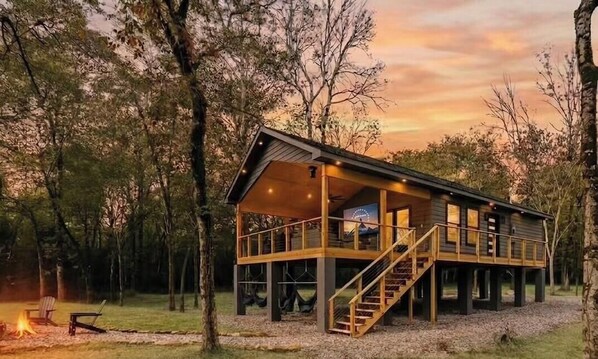 Une cabane en bois dotée d’un balcon, d’un escalier et d’un foyer, située dans une forêt.