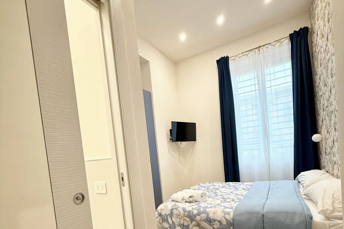 A bedroom with a bed, a TV mounted on the wall, and a window with curtains.