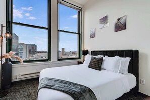 Habitación de hotel con una cama grande, vistas de la ciudad a través de una ventana y dos obras de arte en la pared.