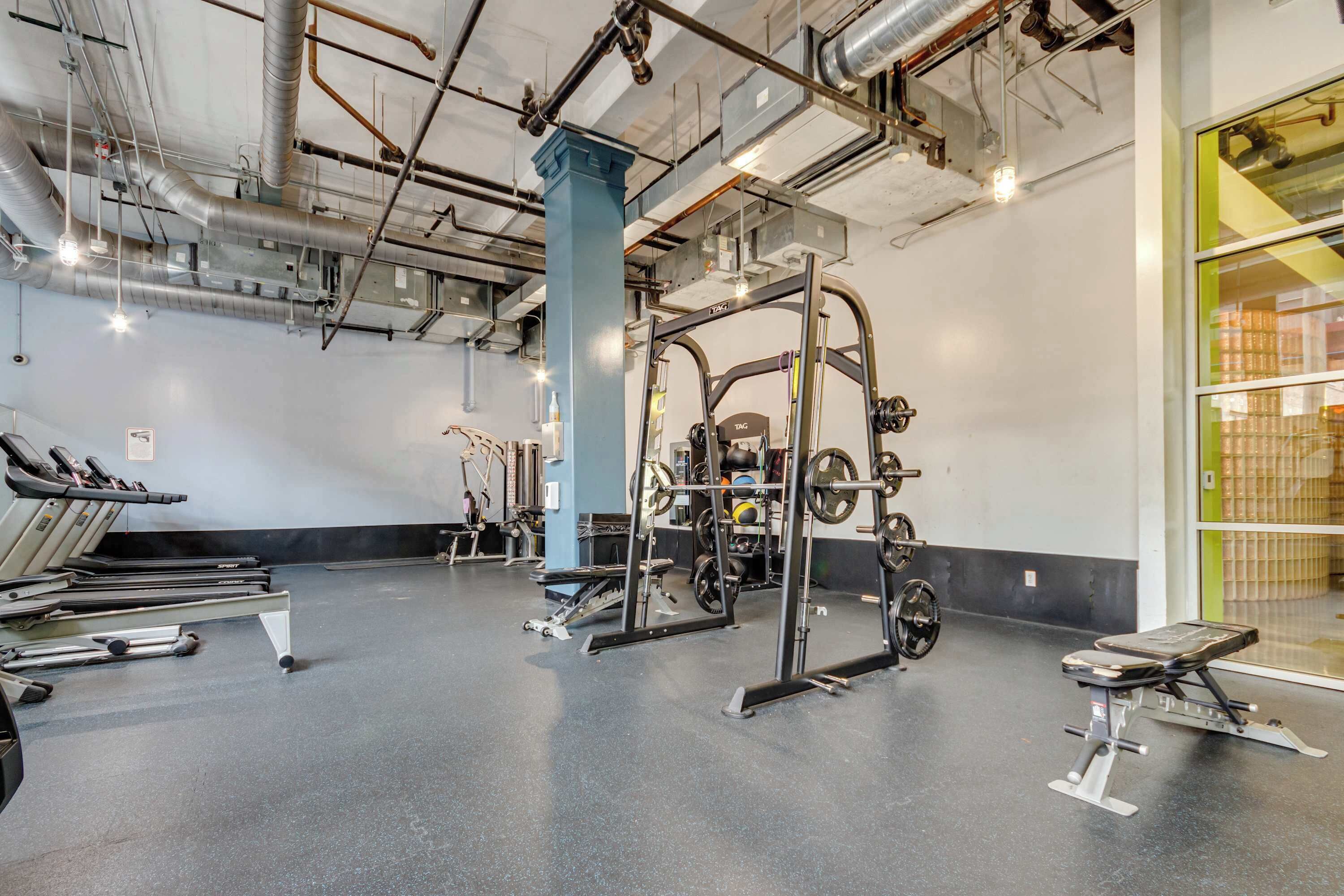 Et fitnesscenter med løbebånd, styrkemaskiner og en squat-stang.