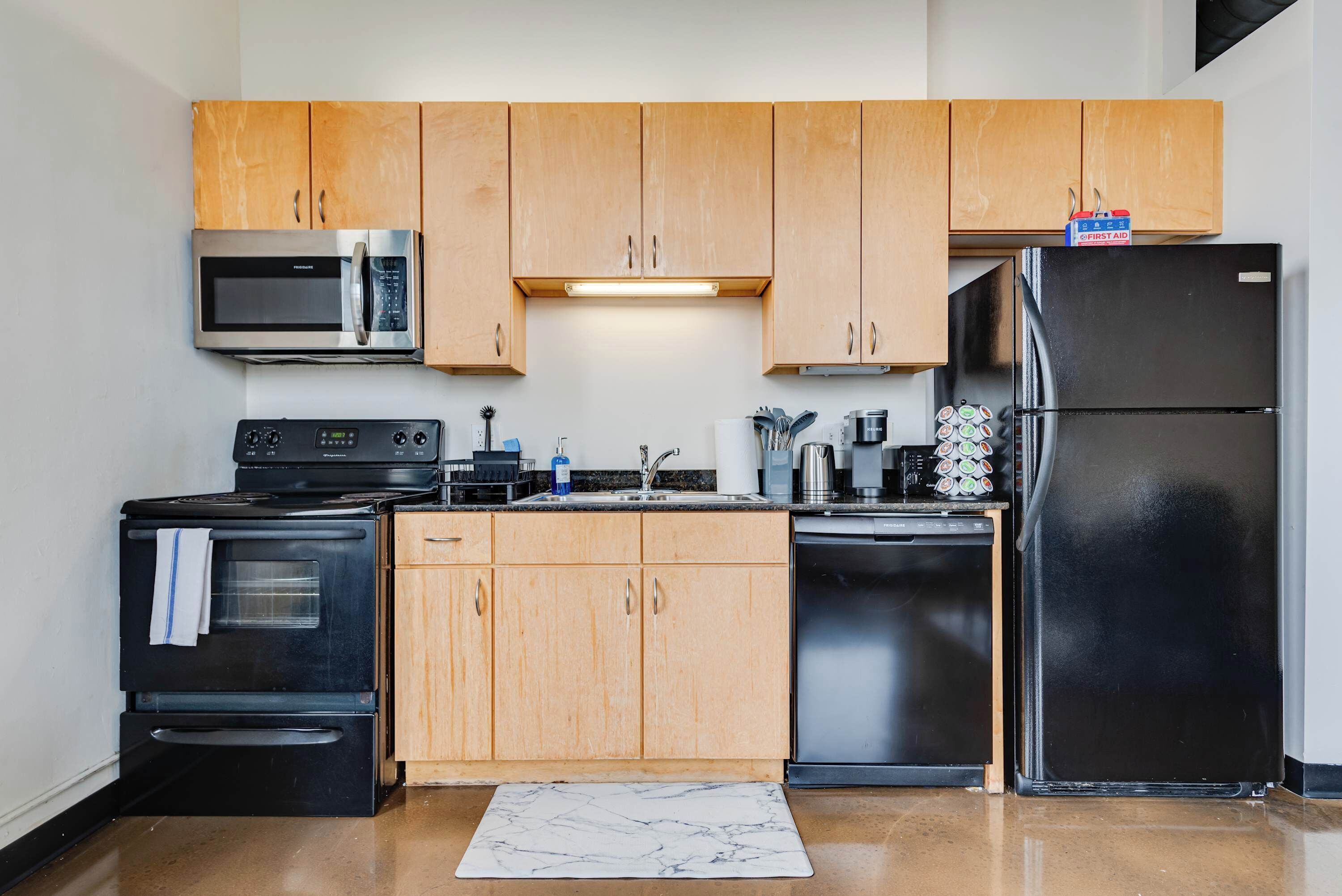 A modern kitchen with wooden cabinets, stainless steel appliances, and a marble floor.