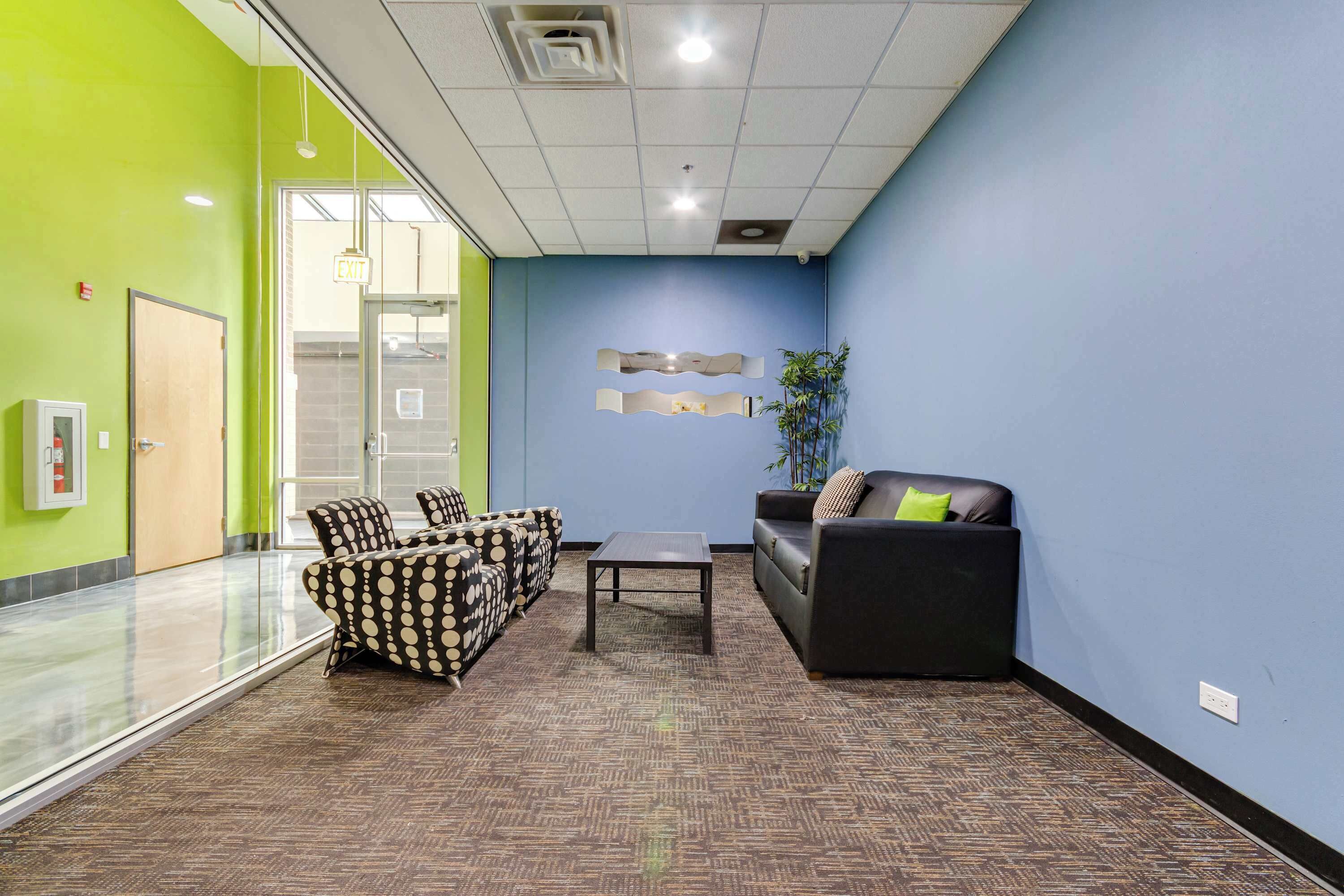 A modern office space with a glass partition, a reception area with a sofa and chairs, and a patterned carpet.
