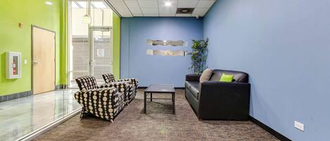 A modern office space with a glass partition, a reception area with a sofa and chairs, and a patterned carpet.