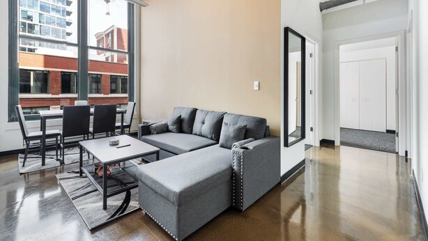 A modern living room with a sectional sofa, a coffee table, and a dining area with chairs and a table. - Modern West Loop Gem-City Views & Prime Location 2 (Chicago)