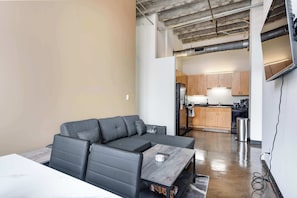 A modern living space with a sectional sofa, a small table, and a kitchenette in the background.