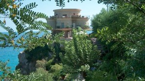 Eine Küstenvilla mit kreisförmiger Struktur, umgeben von üppiger Vegetation mit Blick aufs Meer.