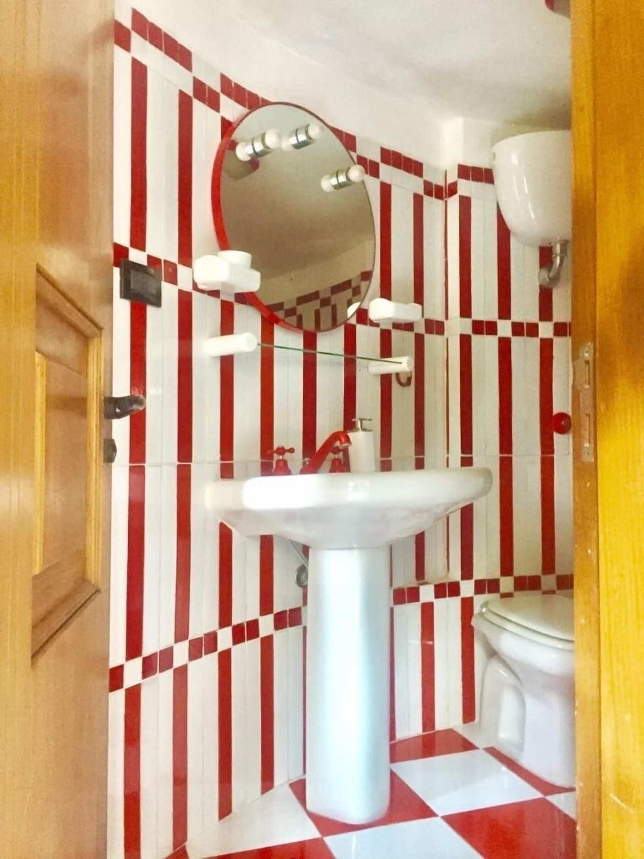 Kylpyhuone, jossa on punavalkoruudullinen lattia, valkoinen pesuallas, peili ja wc-istuin.