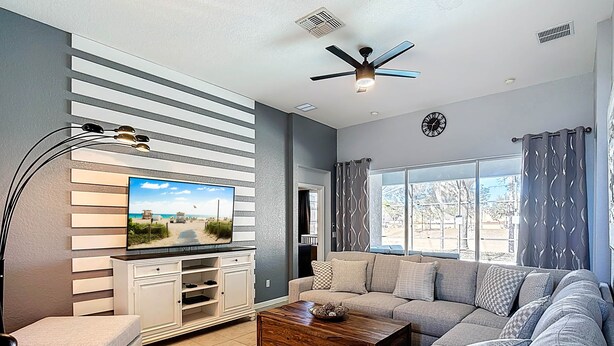 A modern living room with a large flat-screen TV, a ceiling fan, and a large window with curtains. - My Disney Retreat | Free Resort Access-Disney 9min (Four Corners)
