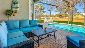 A covered outdoor area with a pool, a blue sofa, and a table. - My Disney Retreat | Free Resort Access-Disney 9min (Four Corners)