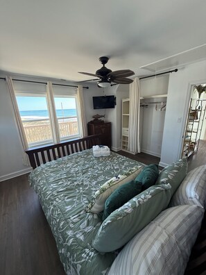 Un dormitorio con cama, ventilador de techo, televisor, armario y vista a la playa.