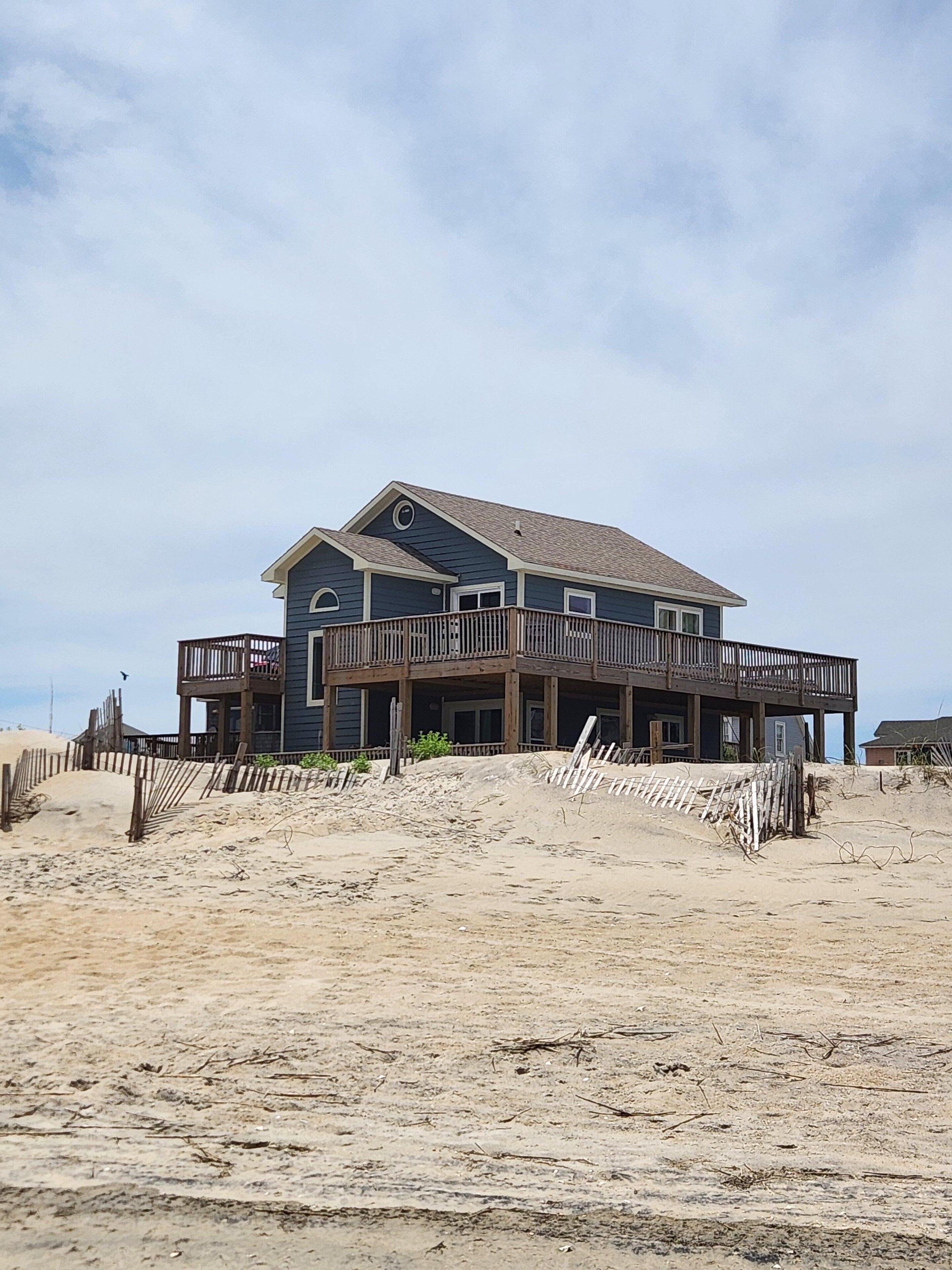 Et toetagers strandhus med balkon, beliggende på en sandstrand.