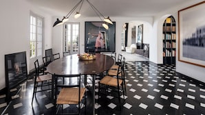 Un coin repas comprenant une table ronde, des chaises, un lustre, une cheminée et une bibliothèque.