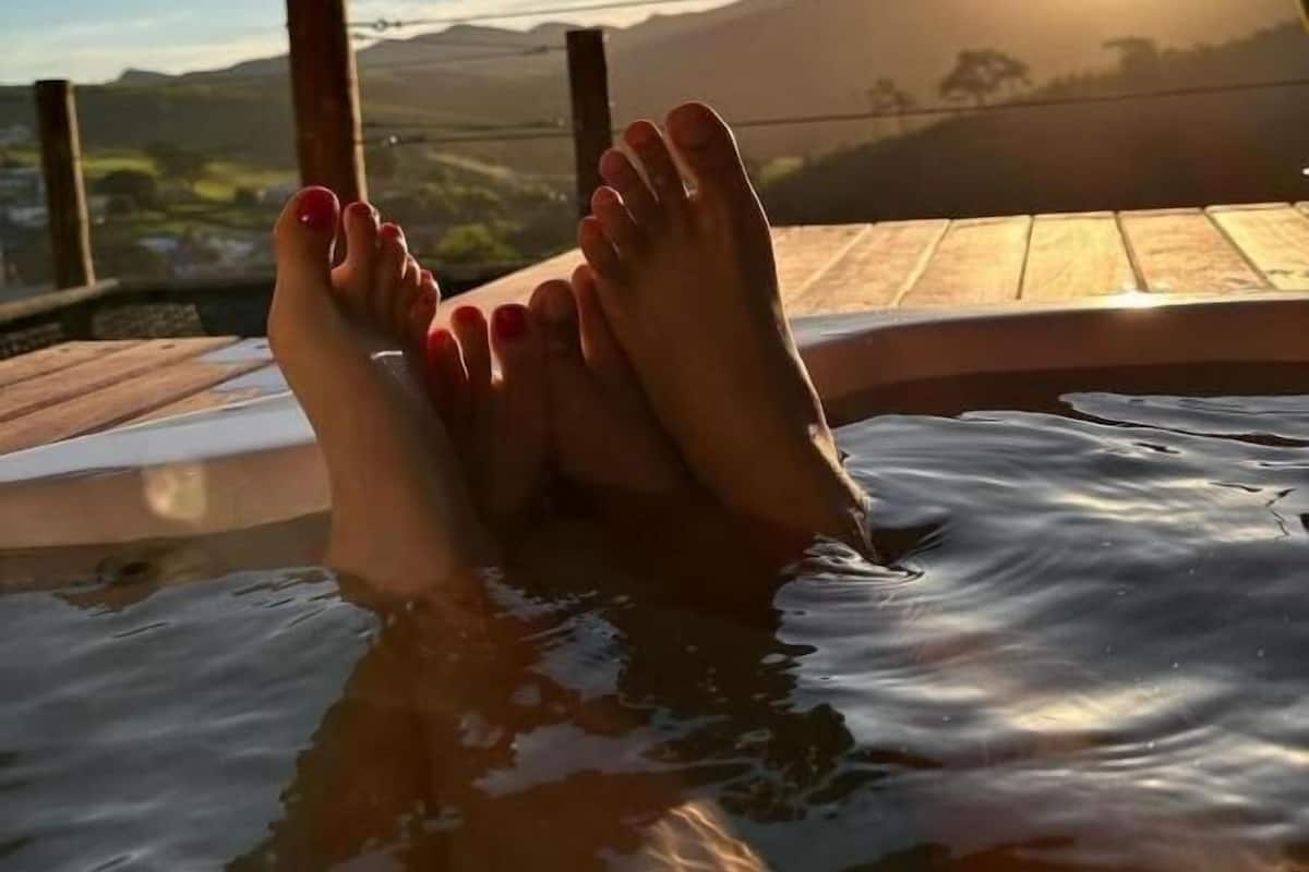 A person relaxing in a hot tub with a scenic view of a sunset and mountains in the background.