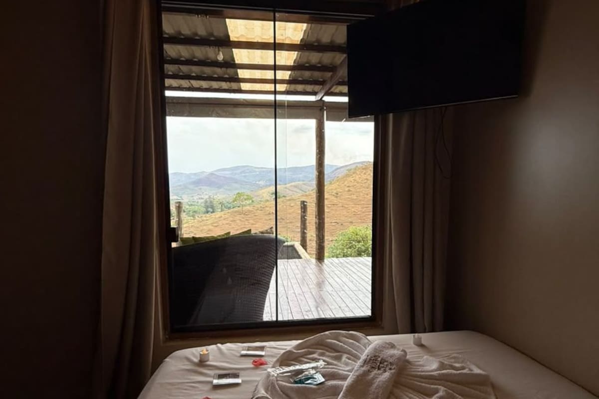 Un dormitorio con cama, ventana con cortinas, televisor de pantalla plana en la pared y vista al exterior.
